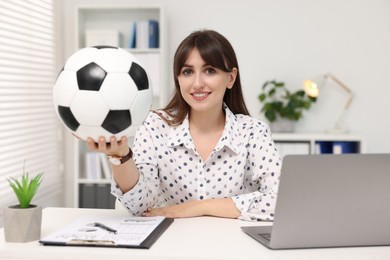 Smiling employee with soccer ball at table in office