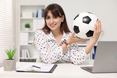 Smiling employee with soccer ball at table in office