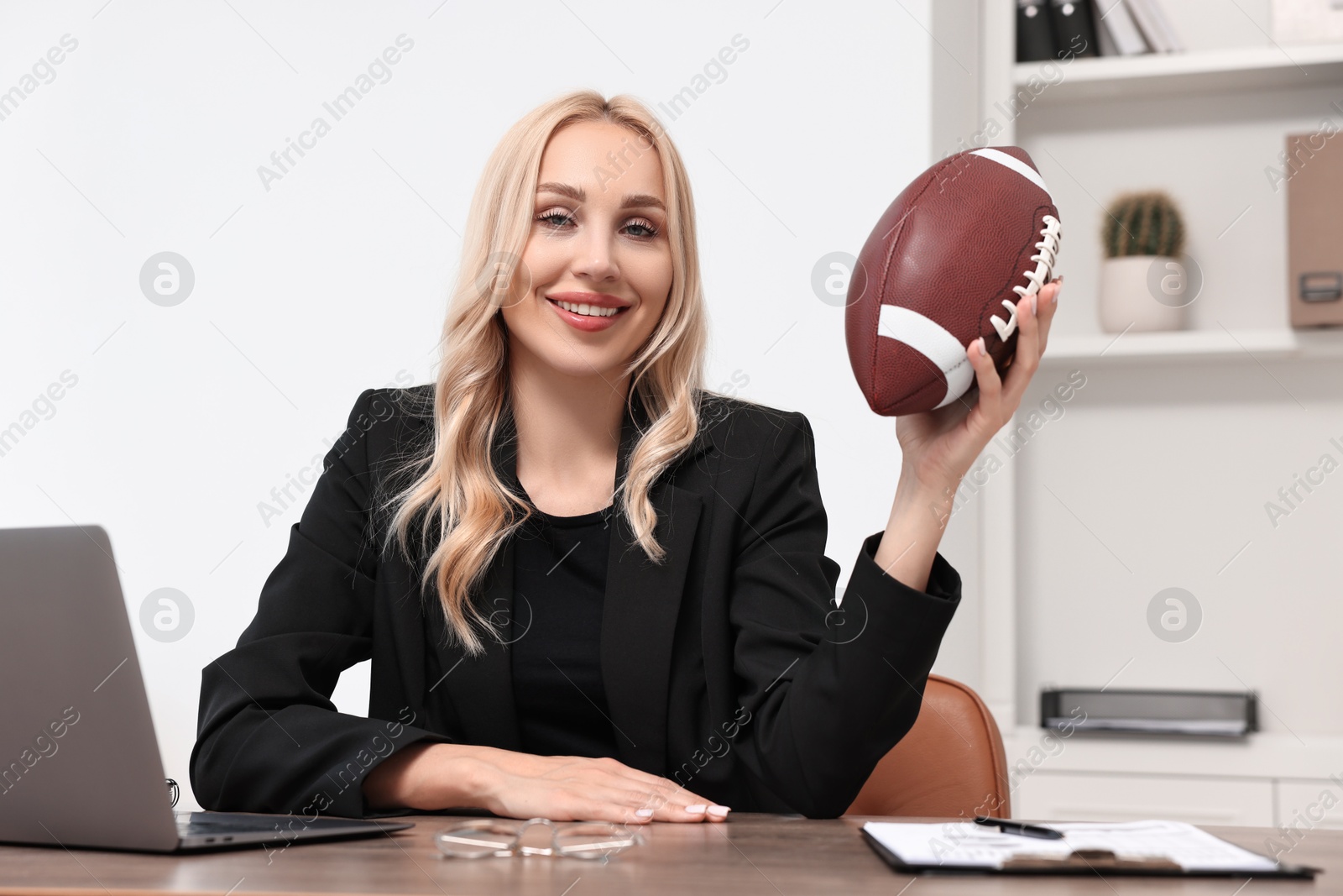 Photo of Happy woman with american football ball at table in office