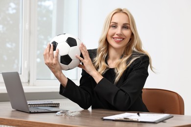 Happy woman with soccer ball at table in office