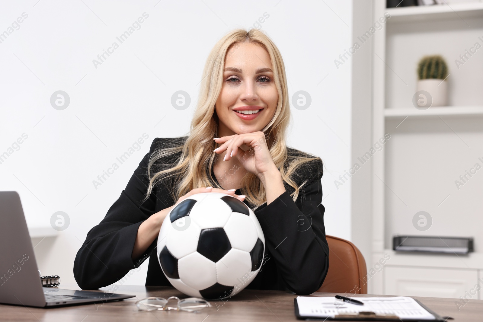 Photo of Happy woman with soccer ball at table in office