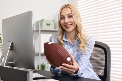 Photo of Happy woman with american football ball at table in office