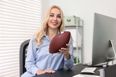 Photo of Happy woman with american football ball at table in office