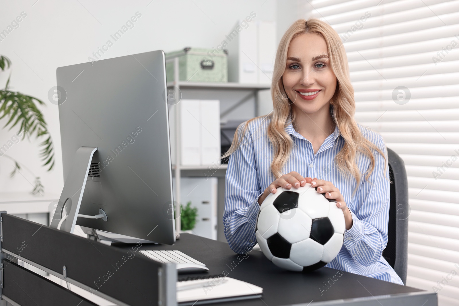 Photo of Happy woman with soccer ball at table in office