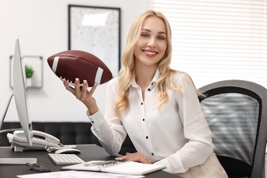 Happy woman with american football ball at table in office