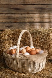 Photo of Fresh chicken eggs in wicker basket on dried straw bale