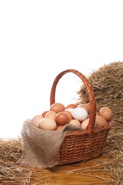 Photo of Wicker basket full of chicken eggs and dried straw on wooden table against white background