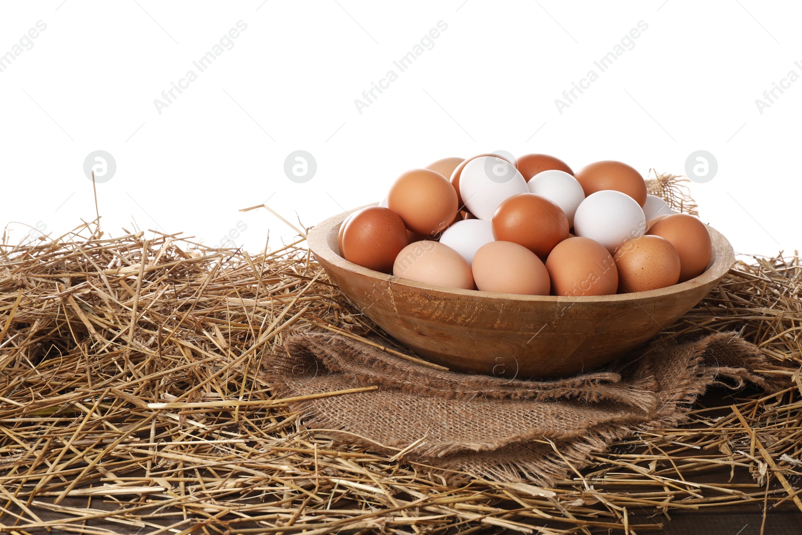 Photo of Fresh chicken eggs in bowl and dried straw on table against white background