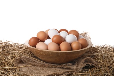 Fresh chicken eggs in bowl and dried straw on table against white background