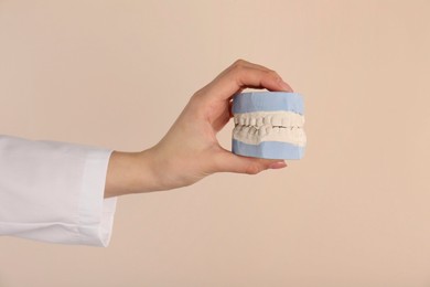 Photo of Doctor holding dental model with jaws on beige background, closeup. Cast of teeth