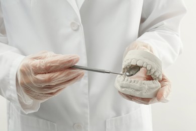 Doctor holding dental model with jaws and tool on white background, closeup. Cast of teeth