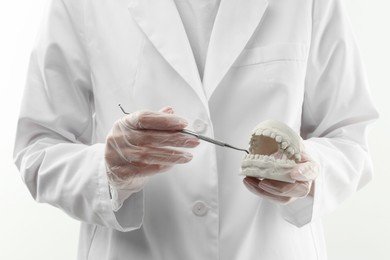 Photo of Doctor holding dental model with jaws and tool on white background, closeup. Cast of teeth