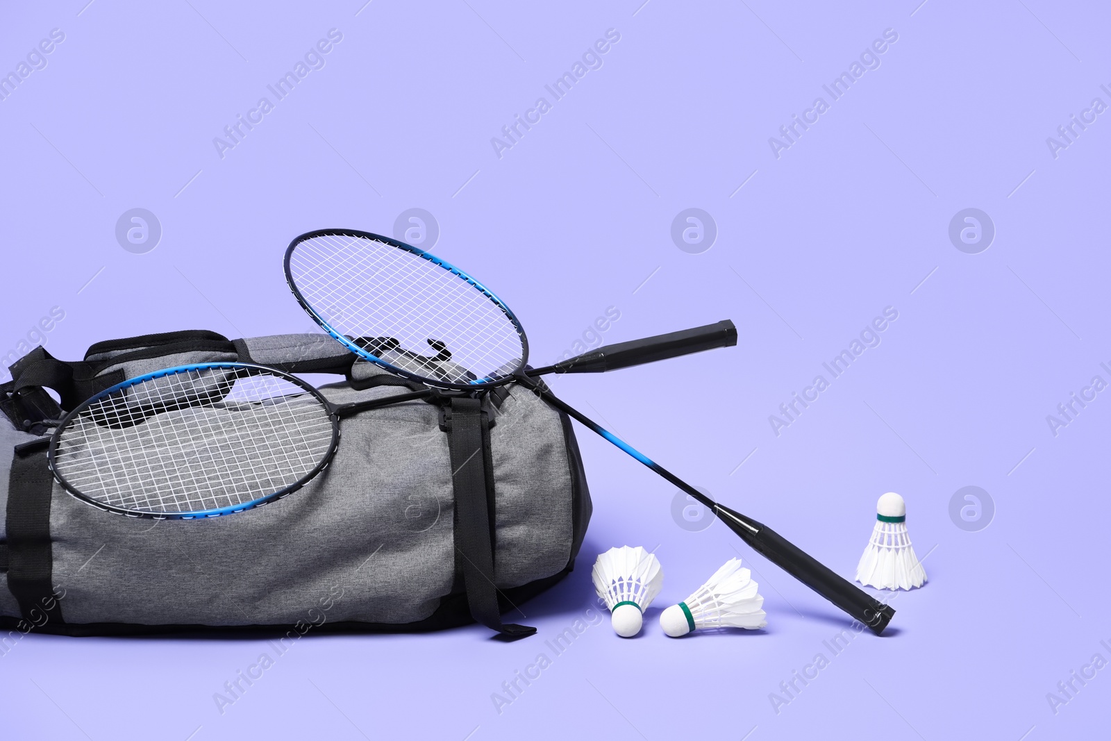 Photo of Feather badminton shuttlecocks, rackets and bag on violet background