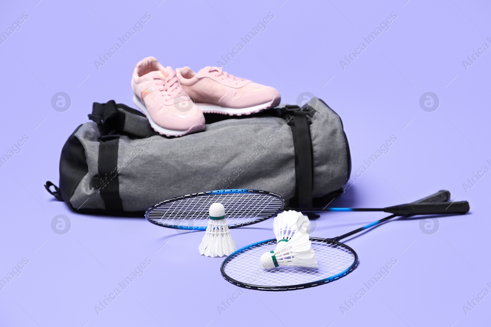 Photo of Feather badminton shuttlecocks, rackets, bag and sneakers on violet background