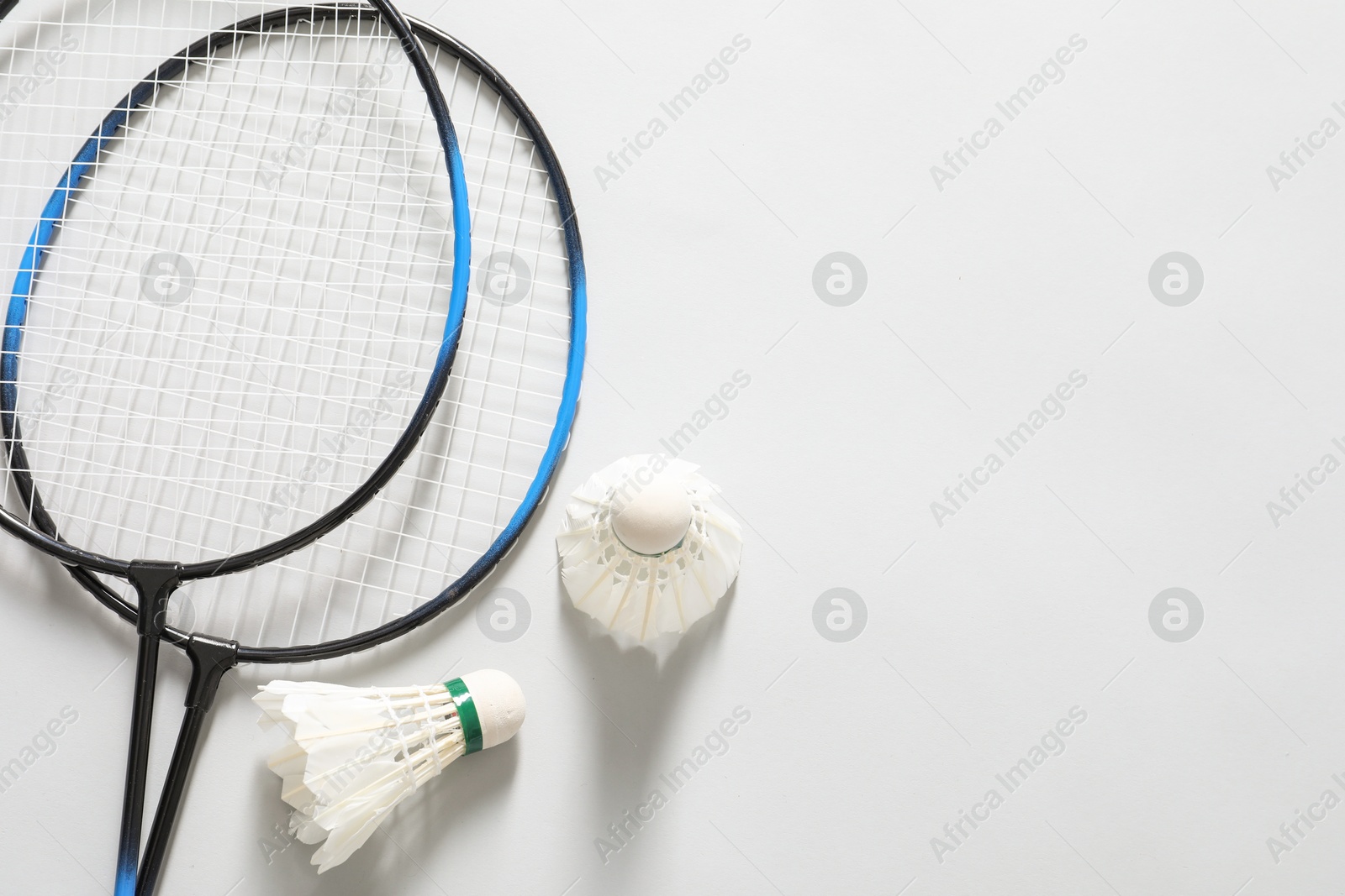 Photo of Feather badminton shuttlecocks and rackets on gray background, flat lay. Space for text