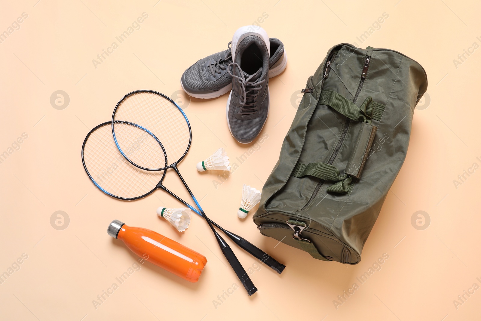 Photo of Badminton set, bag, sneakers and bottle on beige background, flat lay