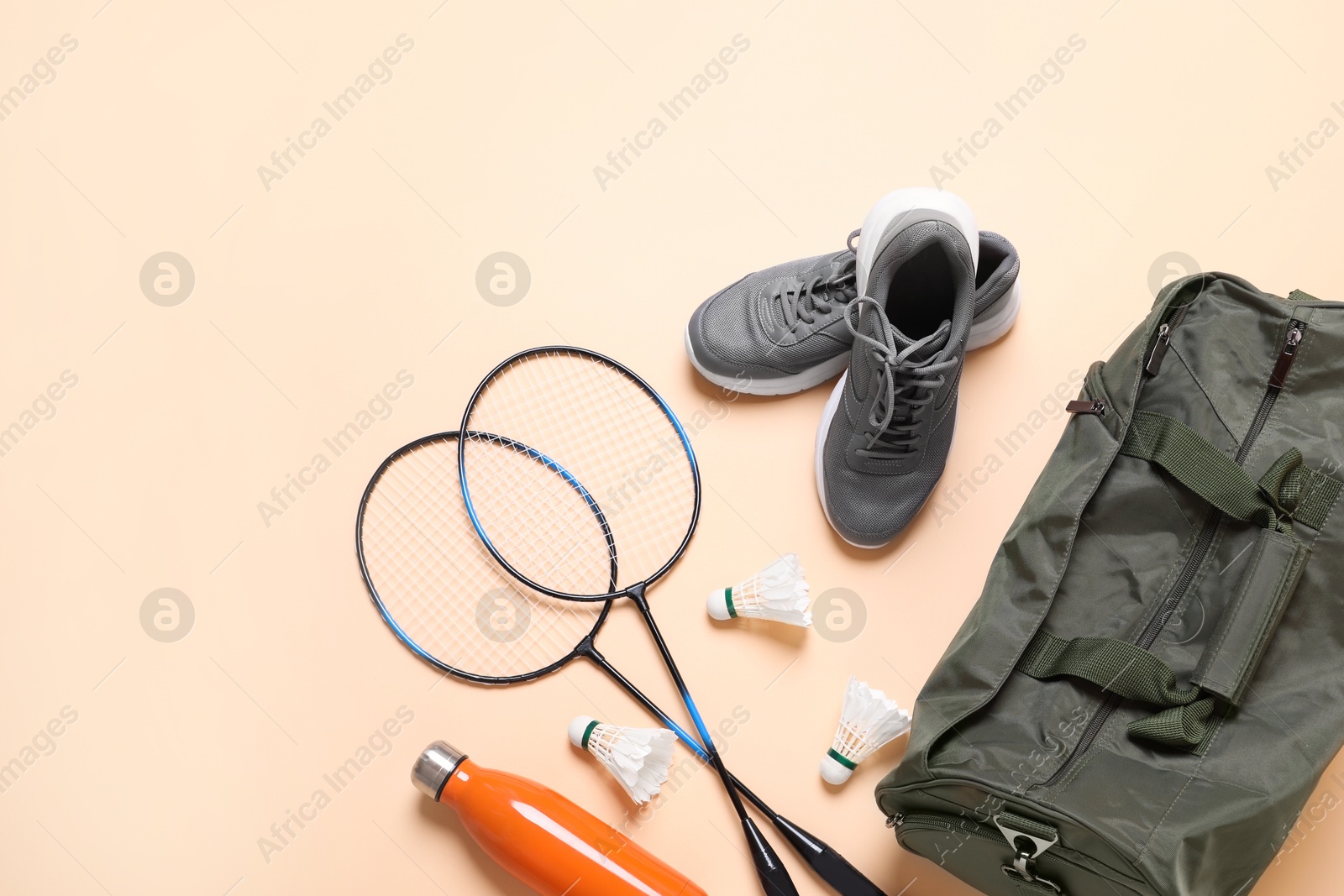 Photo of Badminton set, bag, sneakers and bottle on beige background, flat lay. Space for text