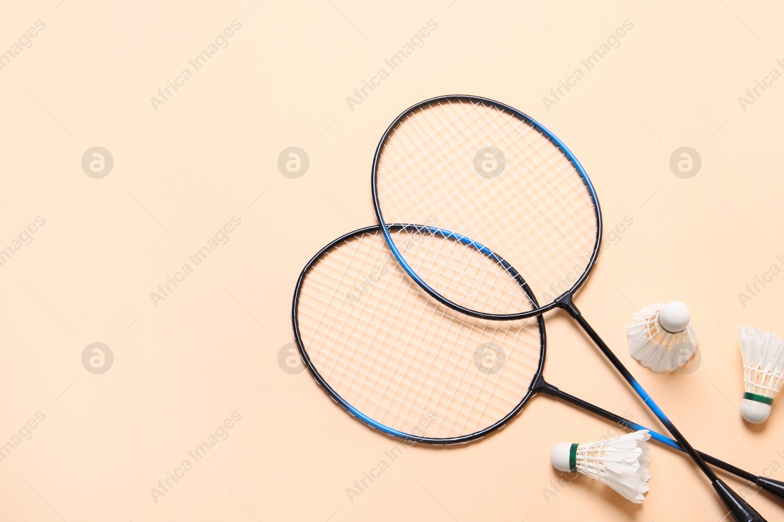 Photo of Feather badminton shuttlecocks and rackets on beige background, flat lay. Space for text