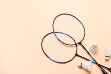 Photo of Feather badminton shuttlecocks and rackets on beige background, flat lay. Space for text