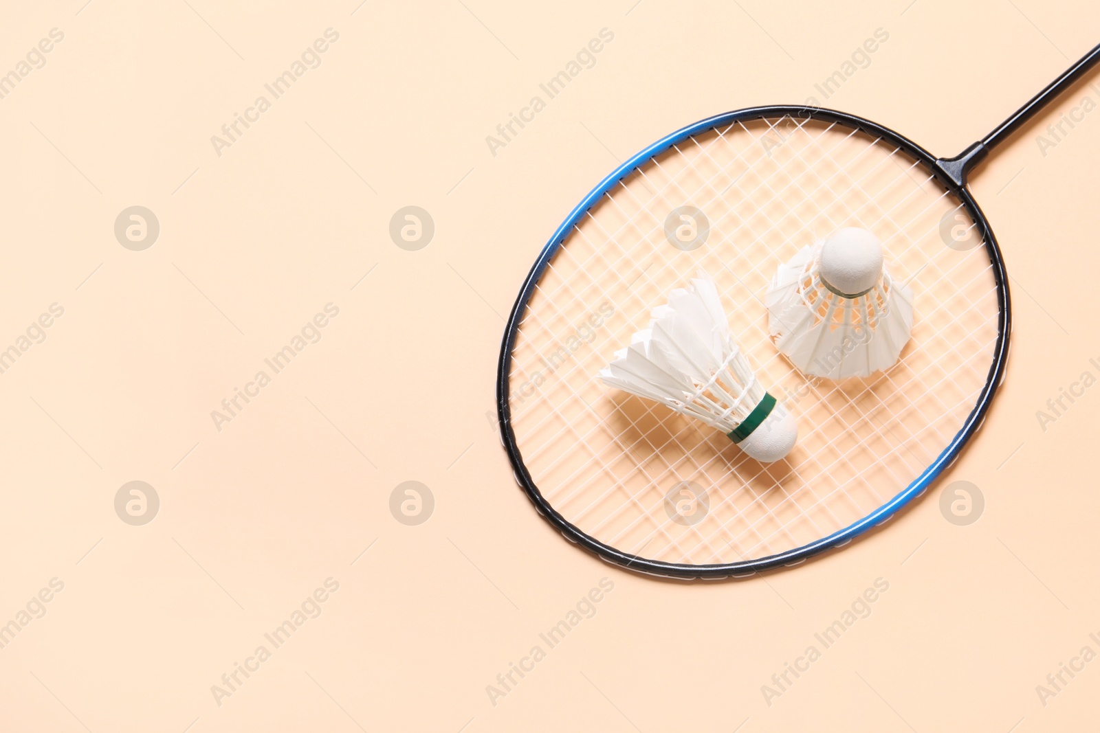 Photo of Feather badminton shuttlecocks and racket on beige background, top view. Space for text