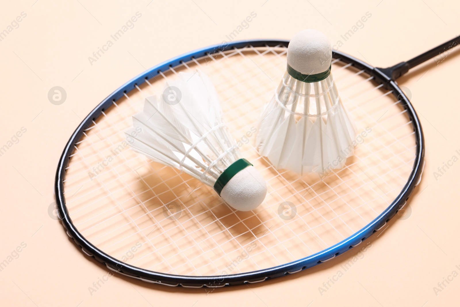 Photo of Feather badminton shuttlecocks and racket on beige background, closeup