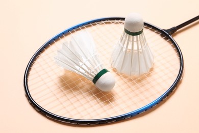Photo of Feather badminton shuttlecocks and racket on beige background, closeup