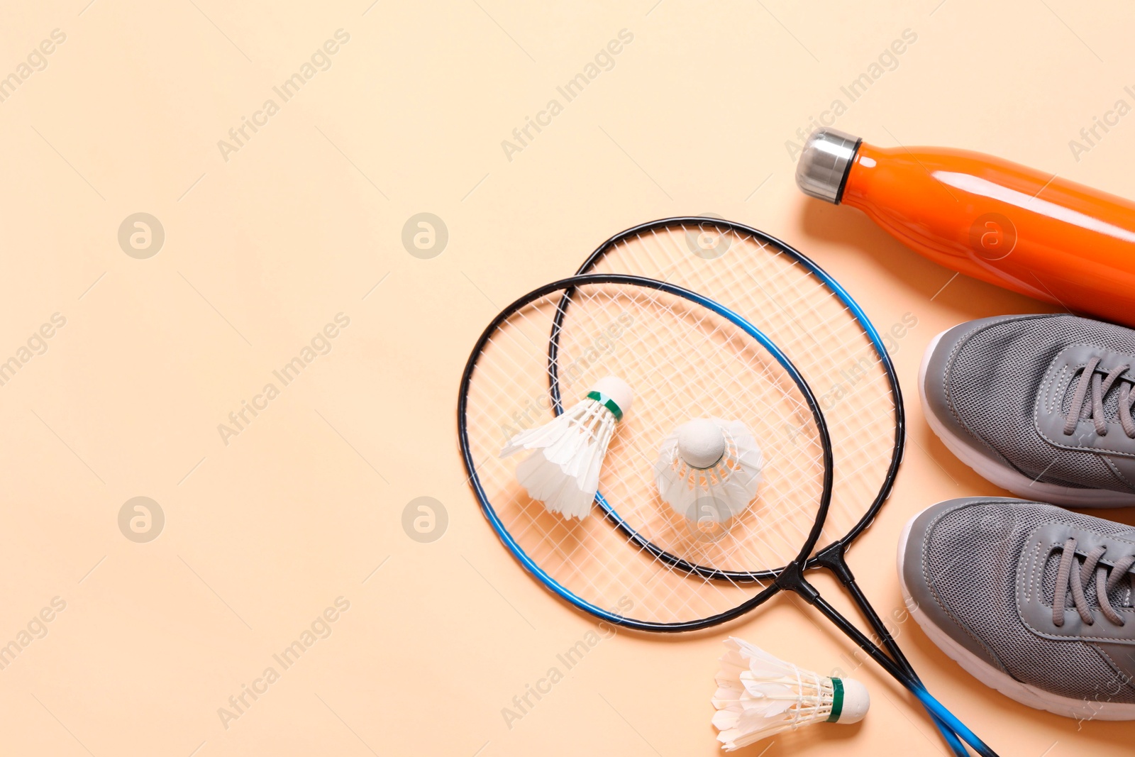 Photo of Feather badminton shuttlecocks, sneakers and bottle on beige background, flat lay. Space for text