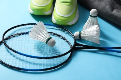 Feather badminton shuttlecocks, rackets and sneakers on light blue background