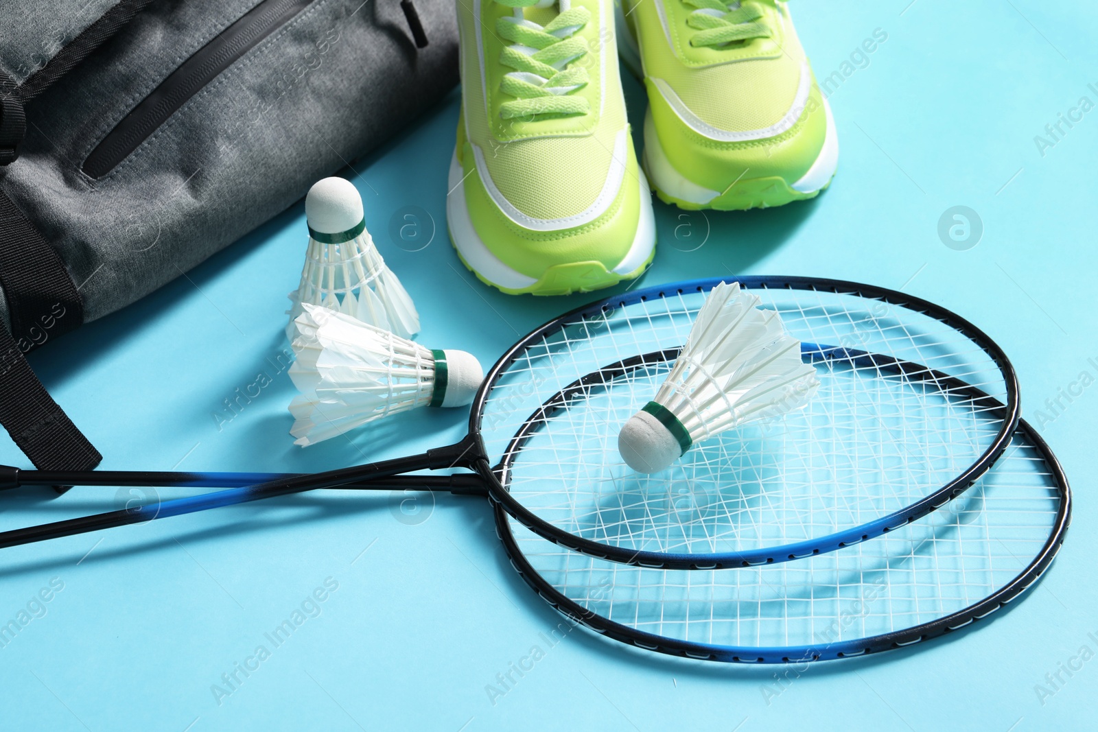 Photo of Feather badminton shuttlecocks, rackets, sneakers and bag on light blue background