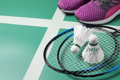 Feather badminton shuttlecocks, rackets and sneakers on court, space for text