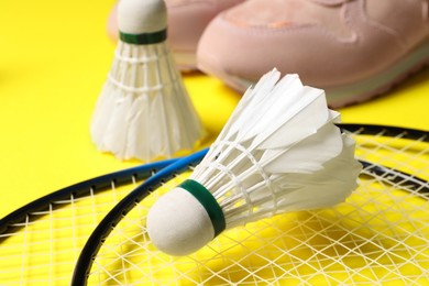 Feather badminton shuttlecocks, rackets and sneakers on yellow background, closeup