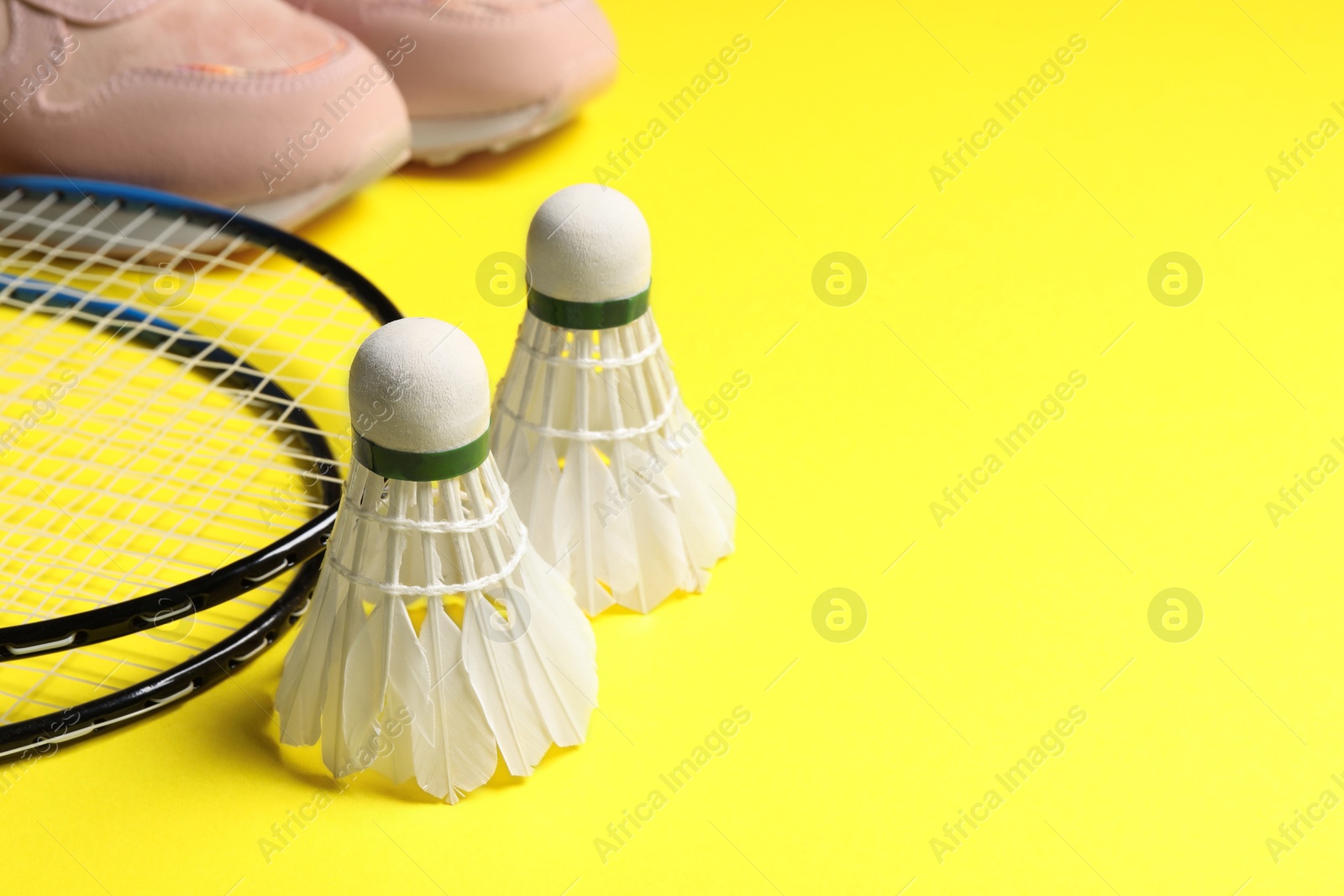 Photo of Feather badminton shuttlecocks, rackets and sneakers on yellow background, closeup. Space for text