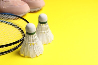 Feather badminton shuttlecocks, rackets and sneakers on yellow background, closeup. Space for text