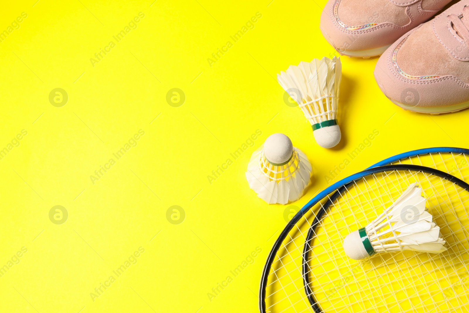 Photo of Feather badminton shuttlecocks, rackets and sneakers on yellow background, above view. Space for text