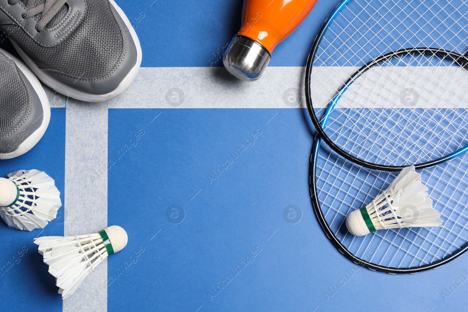 Photo of Feather badminton shuttlecocks, rackets, sneakers and bottle on court, flat lay. Space for text