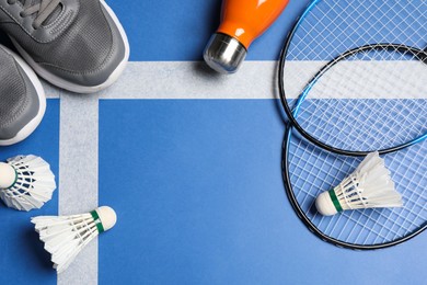 Photo of Feather badminton shuttlecocks, rackets, sneakers and bottle on court, flat lay. Space for text