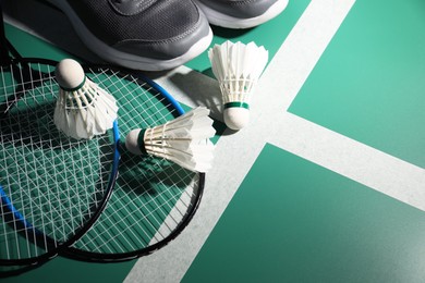 Feather badminton shuttlecocks, rackets and sneakers on court, above view. Space for text