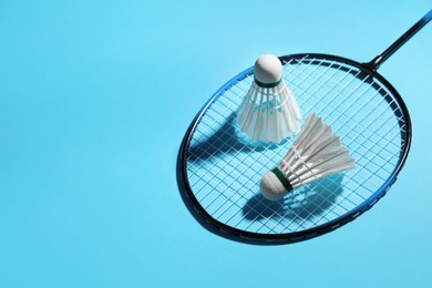 Photo of Feather badminton shuttlecocks and racket on light blue background, space for text