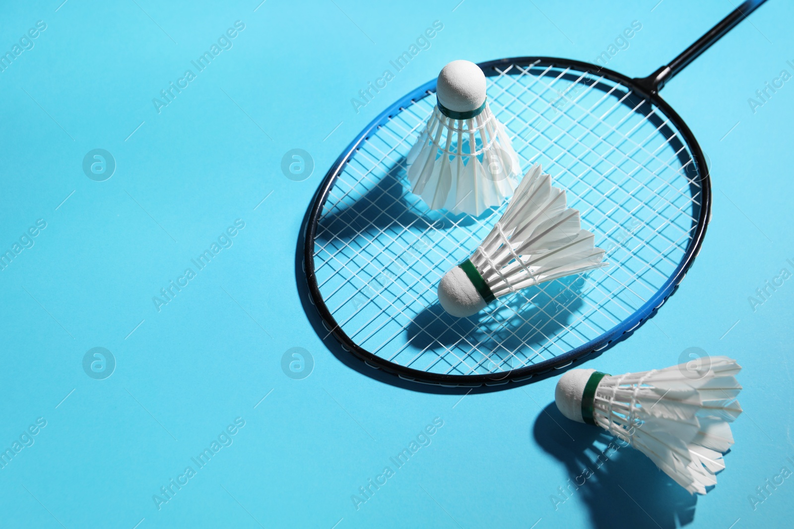 Photo of Feather badminton shuttlecocks and racket on light blue background, space for text