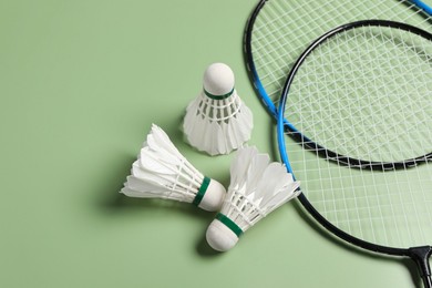 Photo of Feather badminton shuttlecocks and rackets on green background, above view. Space for text