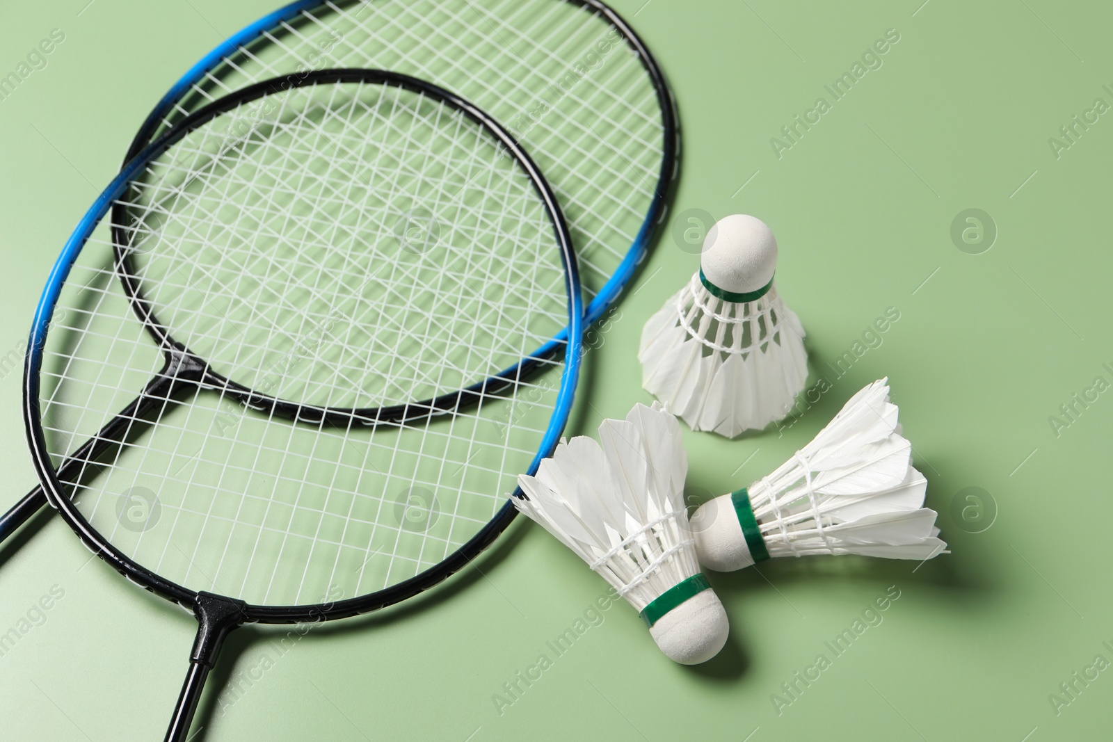 Photo of Feather badminton shuttlecocks and rackets on green background, above view