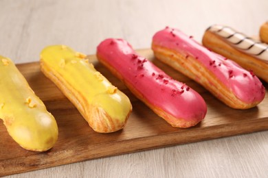 Photo of Board with different tasty glazed eclairs on light wooden table, closeup