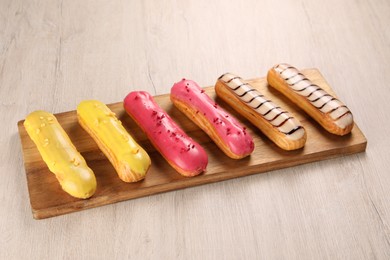 Photo of Board with different tasty glazed eclairs on light wooden table