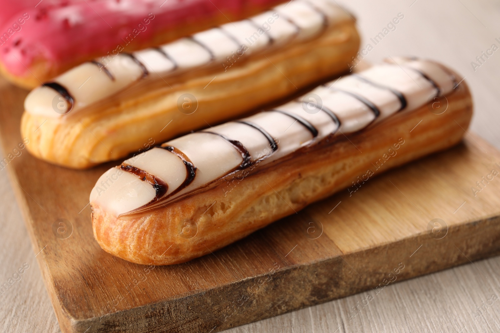 Photo of Board with different tasty glazed eclairs on light wooden table, closeup