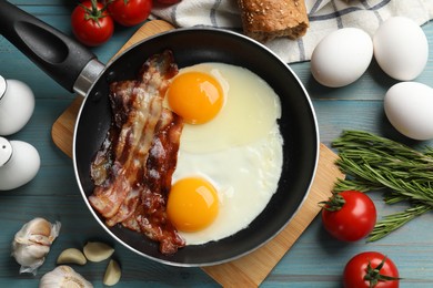 Tasty bacon and eggs in frying pan among products on light blue table, flat lay