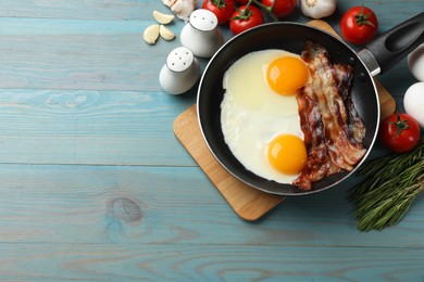 Tasty bacon and eggs in frying pan among products on light blue table, flat lay. Space for text