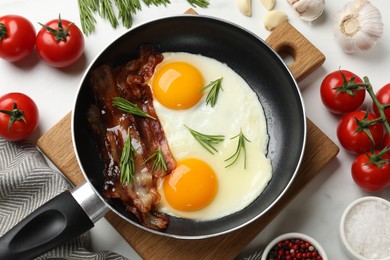 Tasty bacon, eggs and rosemary in frying pan among products on light table, flat lay