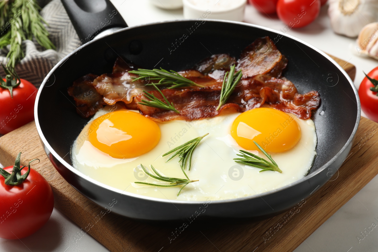 Photo of Tasty bacon, eggs and rosemary in frying pan on light table, closeup