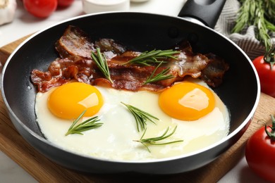 Photo of Tasty bacon, eggs and rosemary in frying pan on light table, closeup