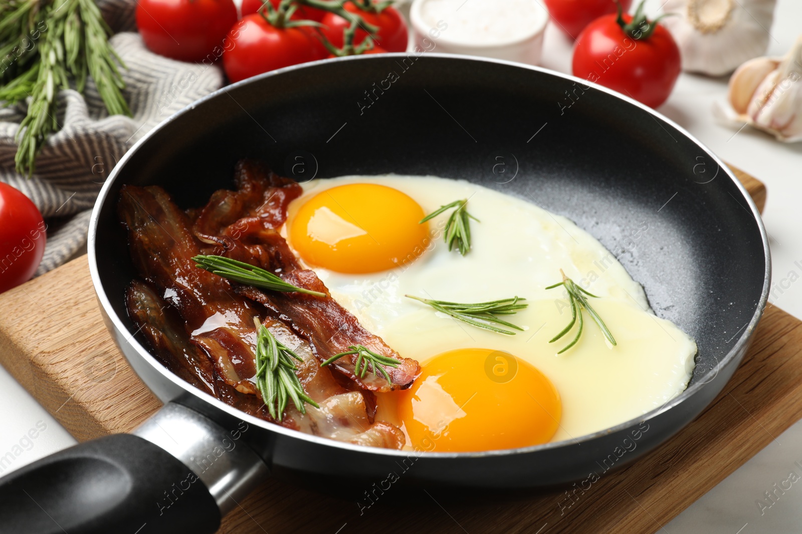 Photo of Tasty bacon, eggs and rosemary in frying pan on light table, closeup